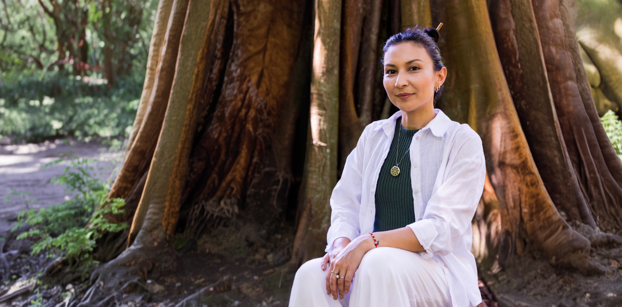 Alyne Yoshida sentada entre as raízes de uma árvore